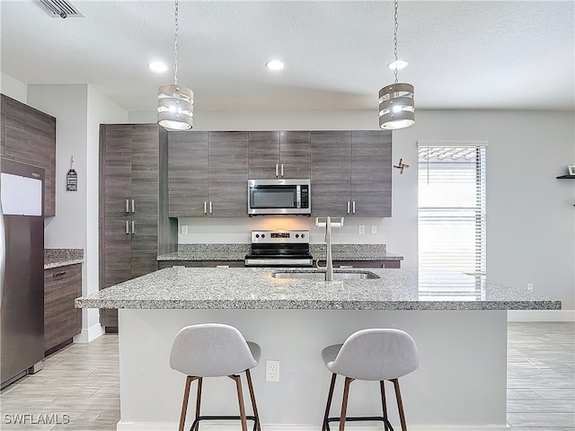 kitchen with light wood-type flooring, appliances with stainless steel finishes, hanging light fixtures, and a breakfast bar