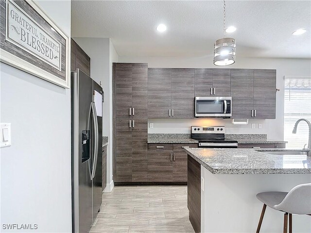 kitchen featuring a textured ceiling, a breakfast bar area, stainless steel appliances, sink, and light wood-type flooring