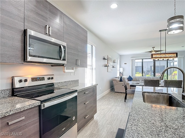 kitchen with light wood-type flooring, stone counters, sink, ceiling fan, and appliances with stainless steel finishes