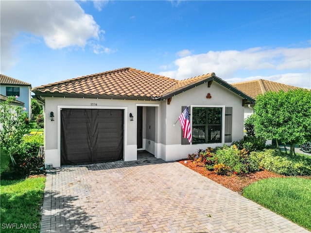 mediterranean / spanish-style home with decorative driveway, a tiled roof, an attached garage, and stucco siding