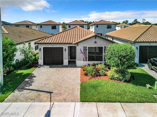 mediterranean / spanish-style house with decorative driveway, stucco siding, a garage, a tiled roof, and a front lawn