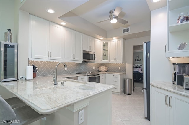 kitchen featuring visible vents, a peninsula, white cabinetry, a sink, and appliances with stainless steel finishes