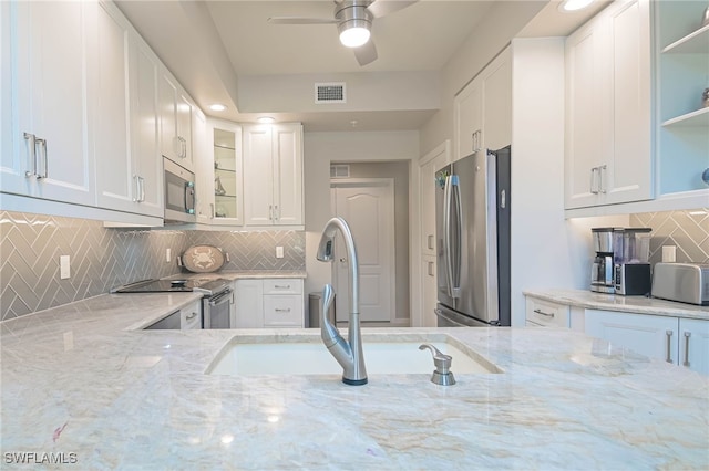 kitchen with stainless steel appliances, light stone counters, sink, and ceiling fan