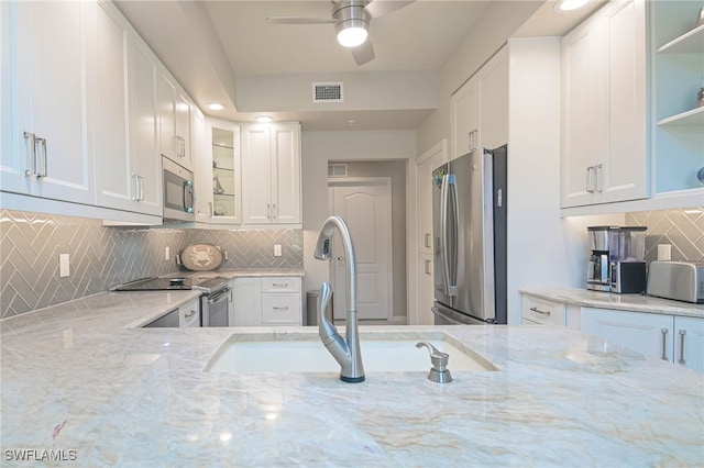 kitchen with backsplash, visible vents, appliances with stainless steel finishes, a sink, and light stone counters