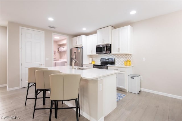 kitchen featuring a sink, washer and dryer, appliances with stainless steel finishes, tasteful backsplash, and a center island with sink