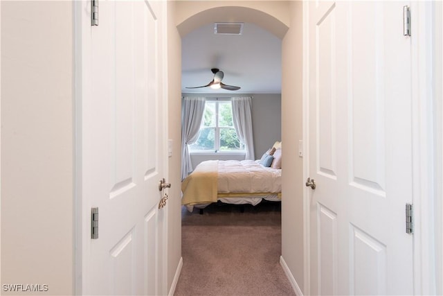 bedroom with arched walkways, dark carpet, visible vents, and baseboards