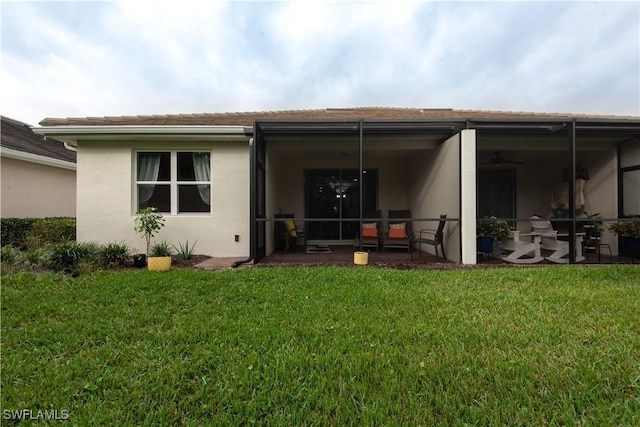 rear view of house with a sunroom, a lawn, and stucco siding