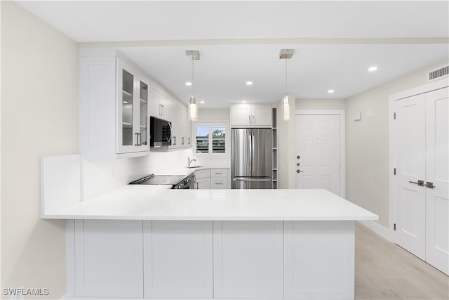 kitchen with a peninsula, stove, a sink, stainless steel fridge, and glass insert cabinets