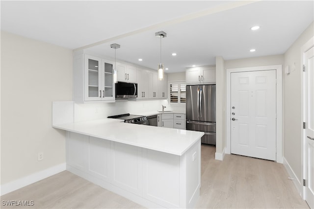 kitchen with light wood-style flooring, glass insert cabinets, a peninsula, stainless steel appliances, and light countertops