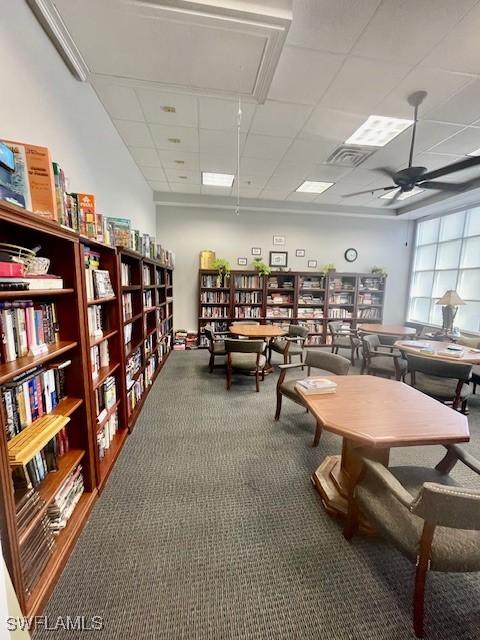 miscellaneous room featuring carpet, visible vents, attic access, wall of books, and a drop ceiling