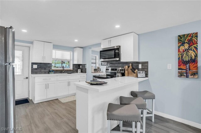 kitchen featuring white cabinets, light wood-type flooring, appliances with stainless steel finishes, a kitchen breakfast bar, and decorative backsplash