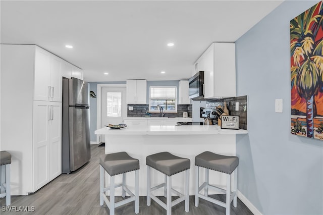 kitchen with light wood-type flooring, tasteful backsplash, stainless steel appliances, kitchen peninsula, and white cabinets