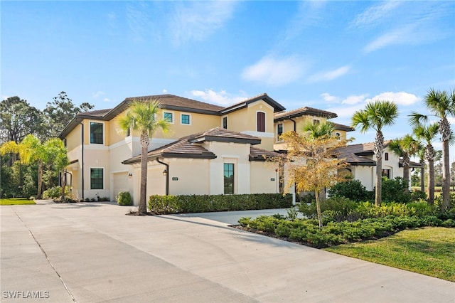 mediterranean / spanish home with concrete driveway, a tile roof, an attached garage, and stucco siding