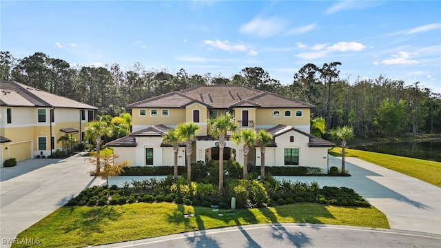 mediterranean / spanish house with driveway, a tile roof, a front yard, and stucco siding