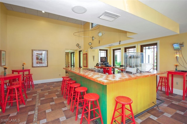 kitchen with a kitchen breakfast bar, a center island, tile countertops, and high vaulted ceiling