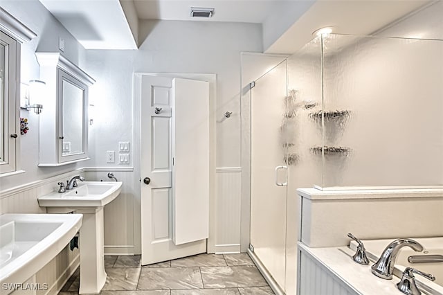 bathroom featuring visible vents, two sinks, wainscoting, a shower stall, and a bath