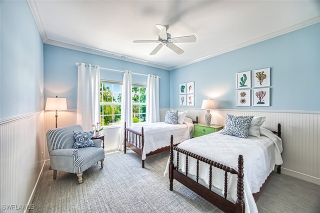 carpeted bedroom featuring a wainscoted wall, ornamental molding, and a ceiling fan