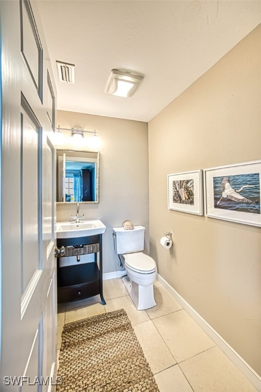 half bath featuring toilet, visible vents, baseboards, vanity, and tile patterned floors