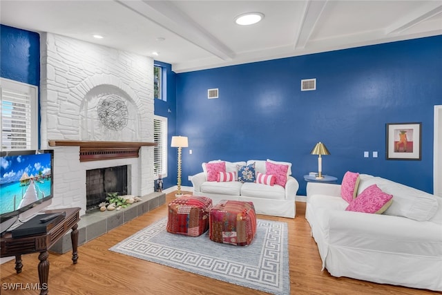 living room featuring wood-type flooring, beam ceiling, and a stone fireplace