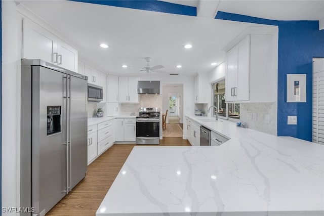 kitchen featuring white cabinetry, hardwood / wood-style flooring, light stone counters, stainless steel appliances, and wall chimney range hood