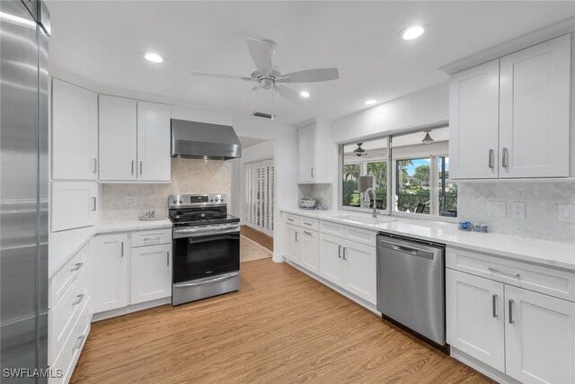 kitchen featuring white cabinetry, appliances with stainless steel finishes, wall chimney range hood, and light hardwood / wood-style flooring