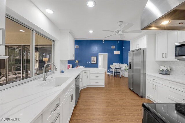 kitchen with appliances with stainless steel finishes, white cabinetry, sink, light stone counters, and light hardwood / wood-style floors