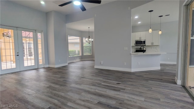 unfurnished living room featuring dark wood-type flooring, ceiling fan with notable chandelier, sink, and french doors