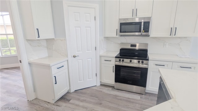 kitchen with white cabinets, light stone countertops, stainless steel appliances, and light hardwood / wood-style flooring