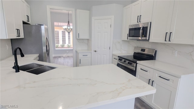 kitchen with appliances with stainless steel finishes, an inviting chandelier, white cabinetry, and sink