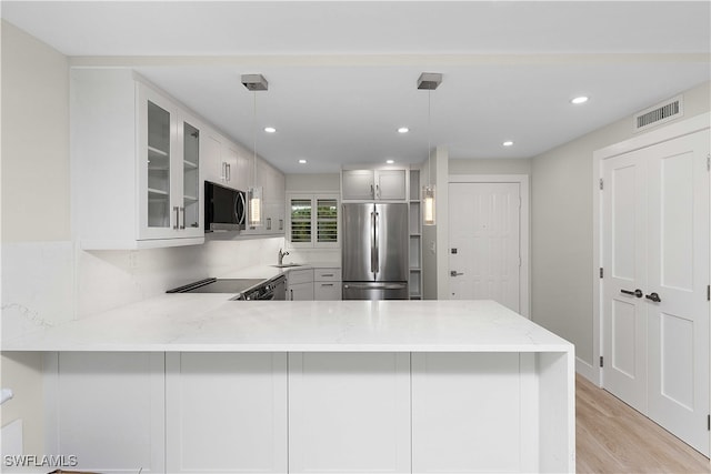 kitchen featuring appliances with stainless steel finishes, glass insert cabinets, a sink, light stone countertops, and a peninsula