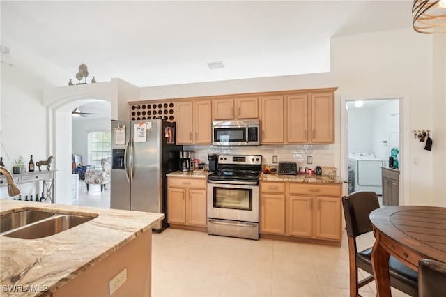 kitchen with tasteful backsplash, sink, washing machine and clothes dryer, appliances with stainless steel finishes, and light stone countertops