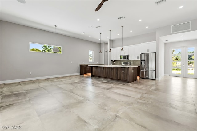 kitchen with decorative light fixtures, ceiling fan, stainless steel appliances, and a center island with sink