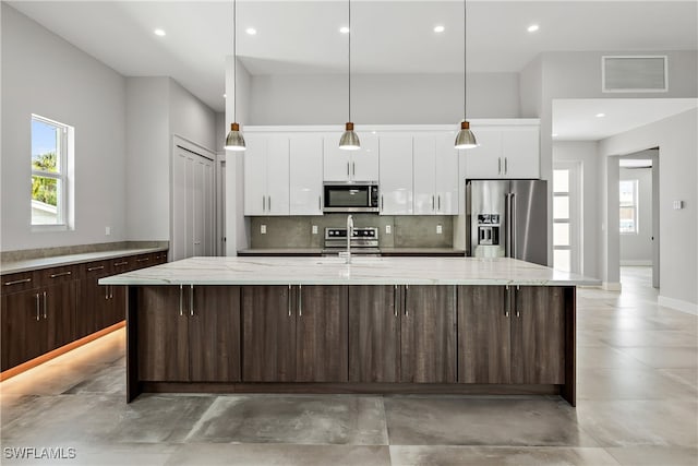 kitchen featuring appliances with stainless steel finishes, an island with sink, white cabinets, and decorative backsplash