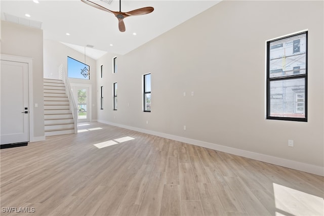 unfurnished living room with light wood-type flooring, ceiling fan, and high vaulted ceiling