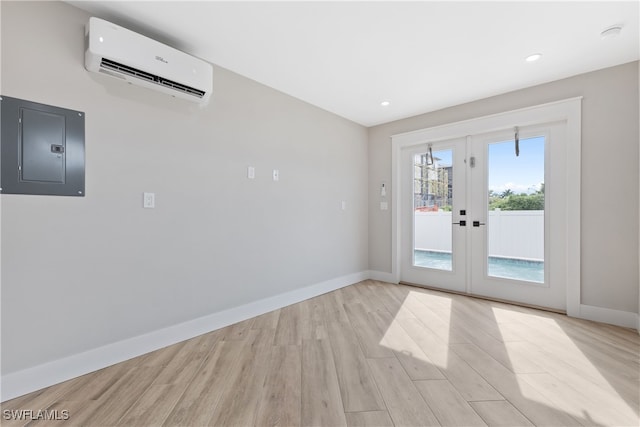 unfurnished room with electric panel, a wall mounted air conditioner, light wood-type flooring, and french doors