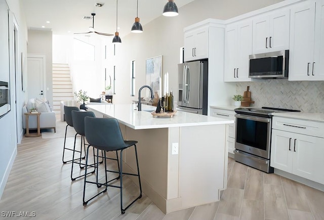 kitchen with pendant lighting, white cabinets, appliances with stainless steel finishes, tasteful backsplash, and a kitchen island with sink