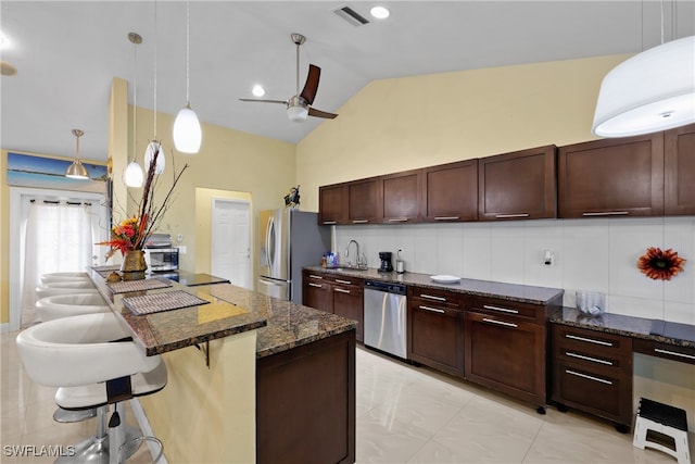 kitchen with stainless steel appliances, dark stone counters, decorative light fixtures, decorative backsplash, and a breakfast bar