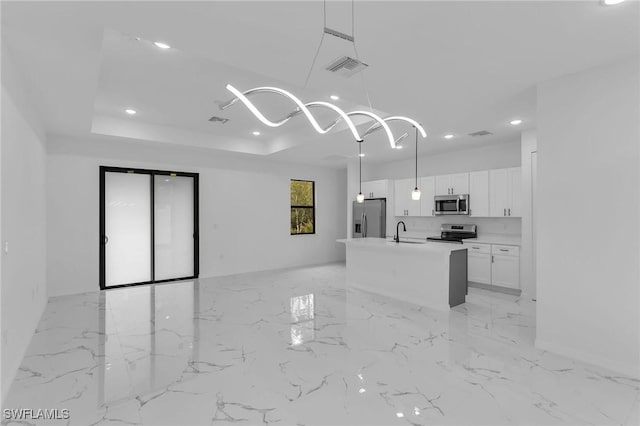 kitchen featuring a raised ceiling, a center island with sink, stainless steel appliances, white cabinetry, and decorative light fixtures