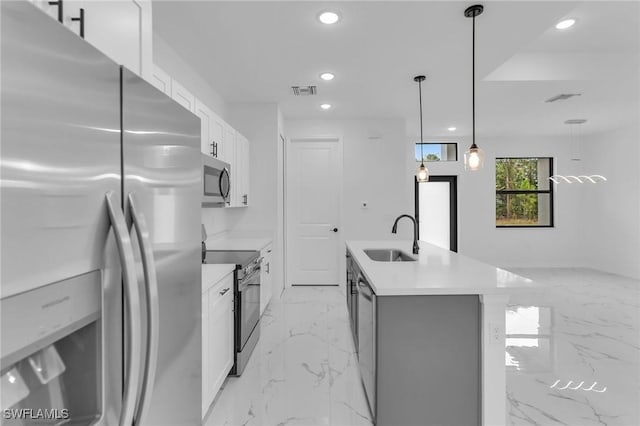 kitchen with white cabinets, stainless steel appliances, an island with sink, hanging light fixtures, and sink