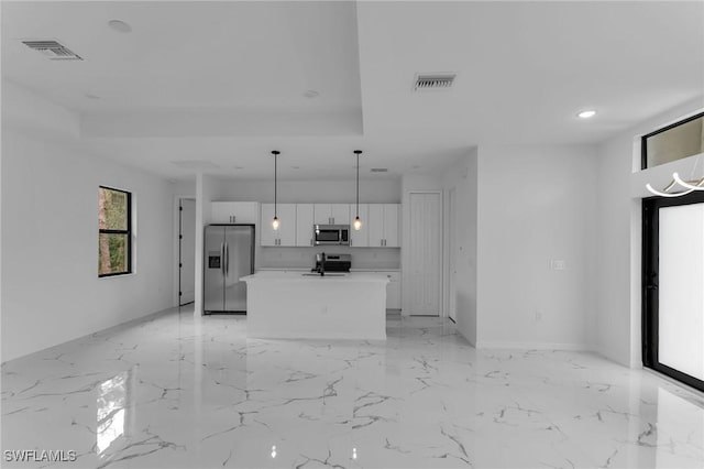 kitchen featuring pendant lighting, stainless steel appliances, a kitchen island with sink, a tray ceiling, and white cabinets