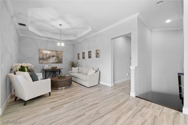 living room with a raised ceiling, light hardwood / wood-style flooring, ornamental molding, and a notable chandelier