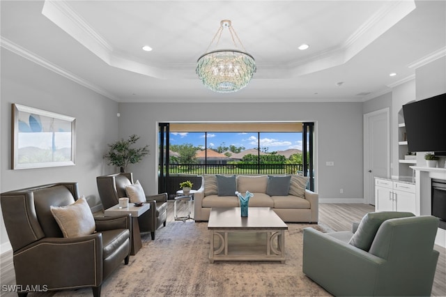 living room featuring an inviting chandelier, a raised ceiling, crown molding, and light hardwood / wood-style flooring