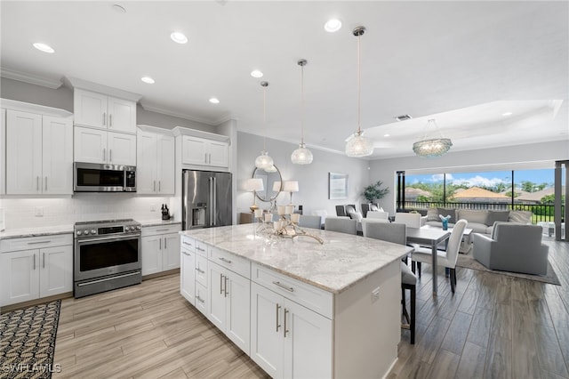 kitchen featuring white cabinets, light hardwood / wood-style floors, decorative light fixtures, a kitchen island, and appliances with stainless steel finishes