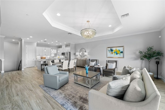 living room featuring a tray ceiling, a chandelier, crown molding, and light hardwood / wood-style floors