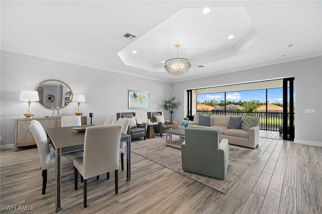 living area featuring a tray ceiling, light wood-type flooring, visible vents, and an inviting chandelier