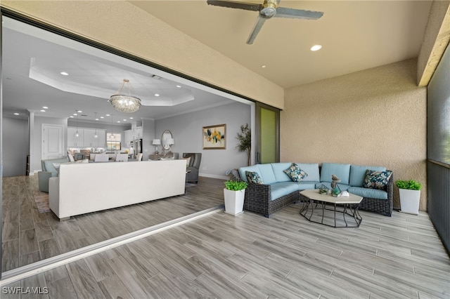 living room with a raised ceiling, ceiling fan, light hardwood / wood-style flooring, and crown molding