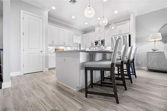 kitchen featuring crown molding, visible vents, white cabinets, stainless steel microwave, and pendant lighting