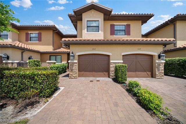 mediterranean / spanish-style house with stone siding, decorative driveway, and stucco siding