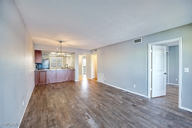 unfurnished living room featuring dark wood-type flooring, a textured ceiling, and a notable chandelier