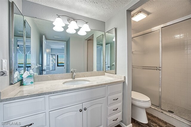 bathroom with toilet, vanity, a textured ceiling, hardwood / wood-style flooring, and a shower with shower door